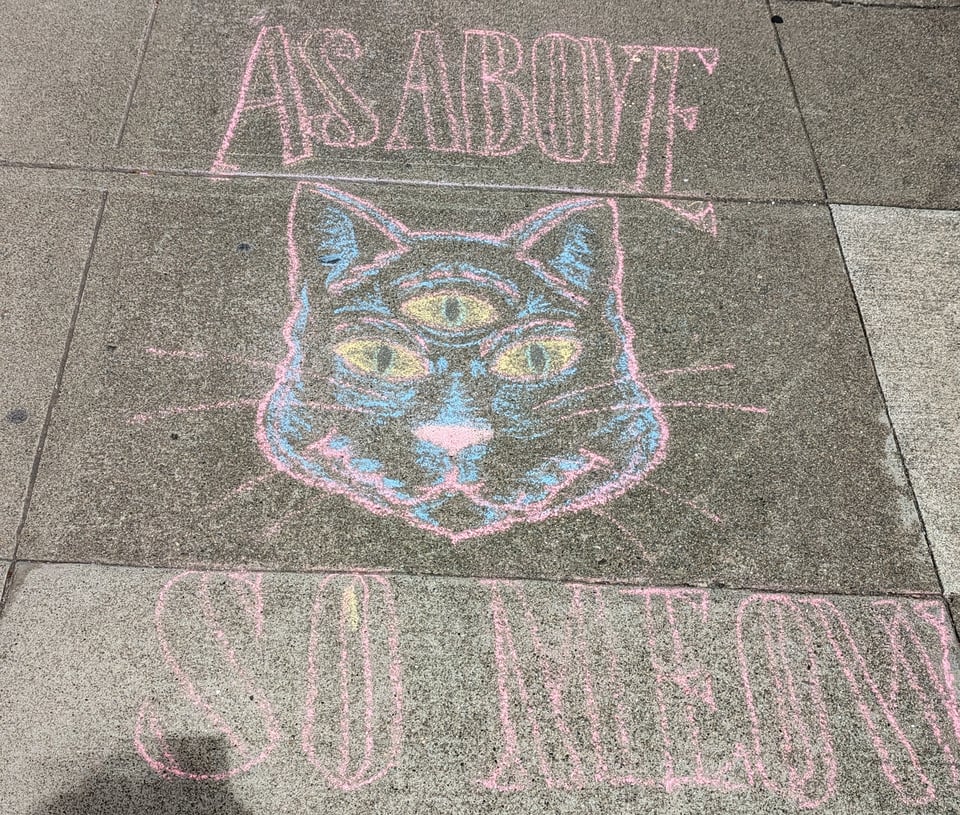Chalk on a sidewalk depicts a three-eyed cat, and it says "AS ABOVE SO MEOW"
