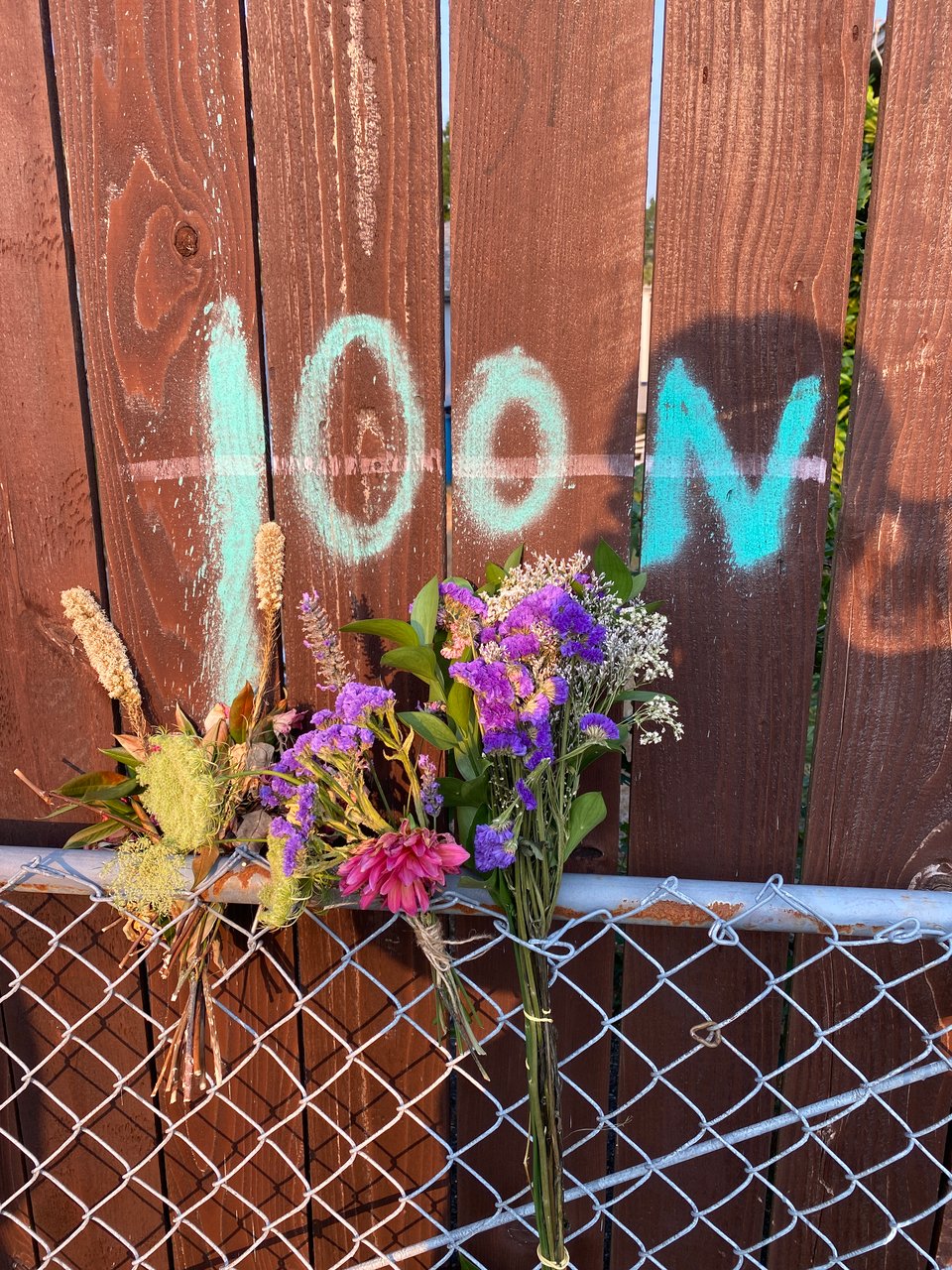 graffiti tag on a fence that reads, “loon” with flowers placed in front of it.