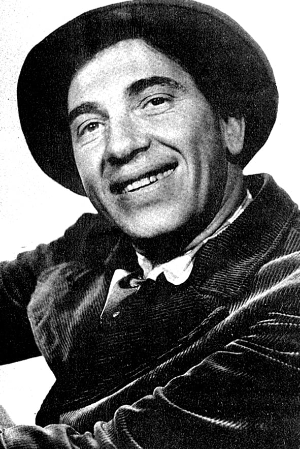 black-and-white movie still of a white man wearing a rumpled suit and hat