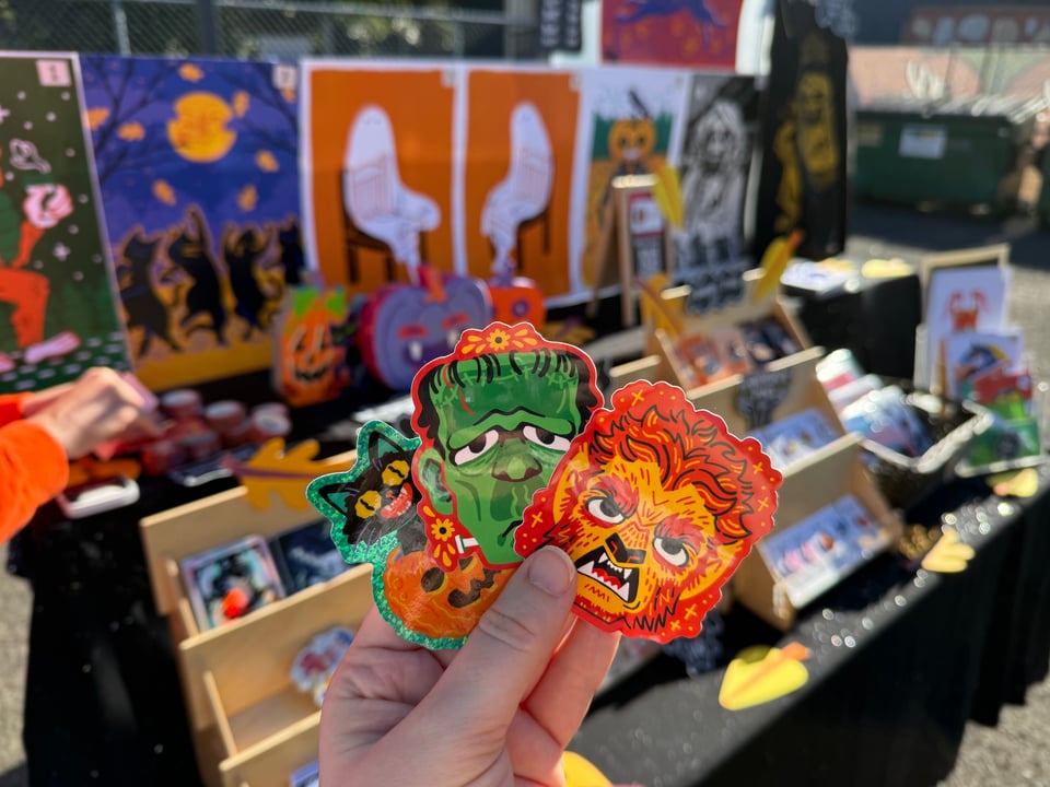 A person holds up monster stickers in front of a display of art prints.