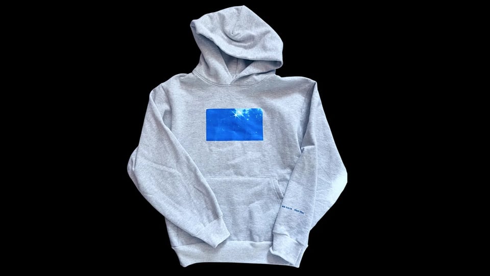 A gray hoodie with a picture of the cover screenprinted on it and turned horizontally across the chest.