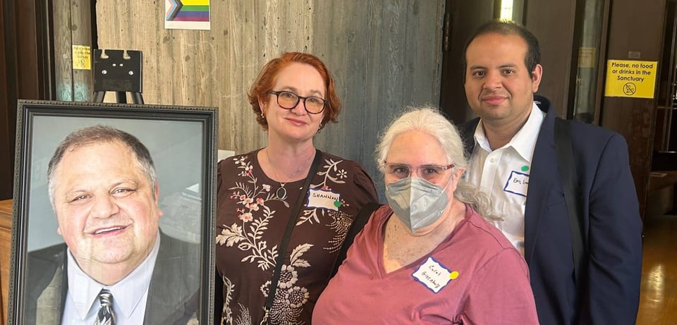 Photo of Shannon Rosa, Carol Greenburg, and Eric Garcia, taken next to a framed photo of Steve at his memorial service.