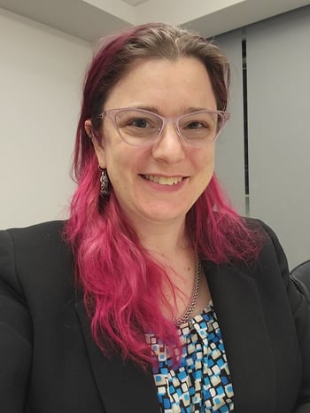 Meredith is wearing a blazer and shell and smiling at the camera. Her hair is brown on top and pink on the bottom.