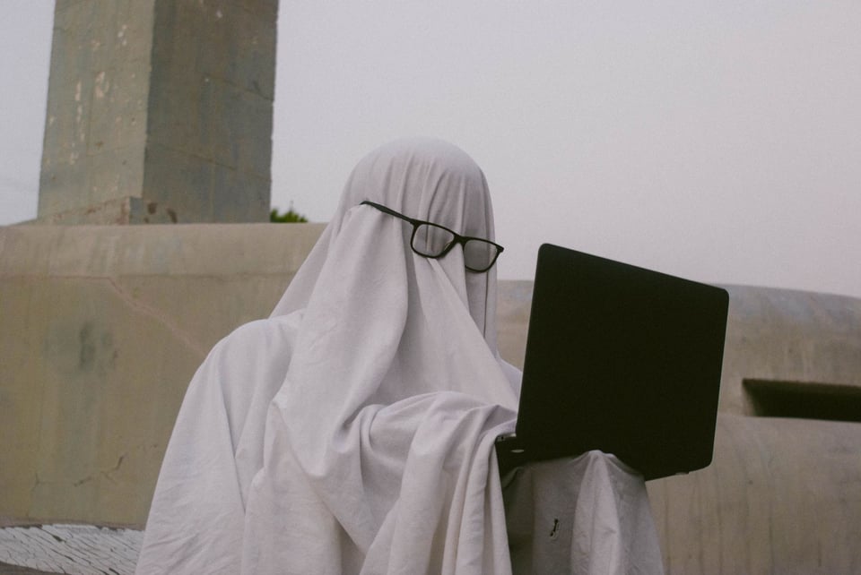 A person wearing a ghost costume and eyeglasses holding a laptop
