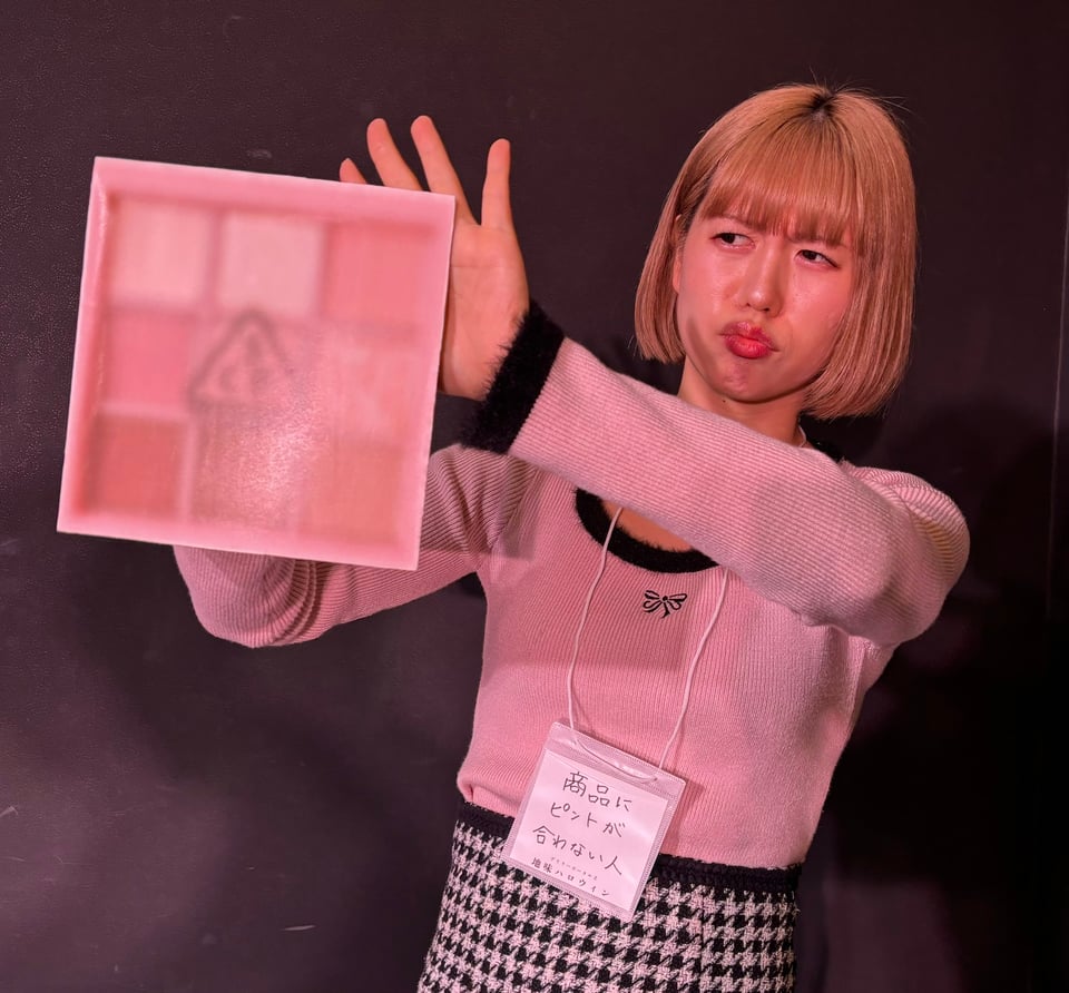 A woman holds up a large, blurry picture of a makeup compact