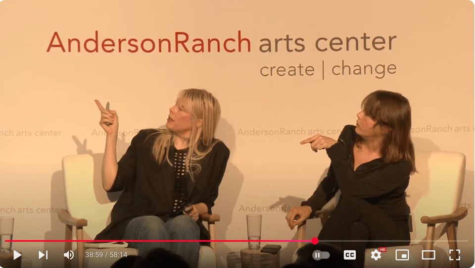 Johanna Fateman and Issy Wood seated beneath signage reading "AndersonRanch arts center." Both wear black and are pointing to someting out of the frame, to their right.