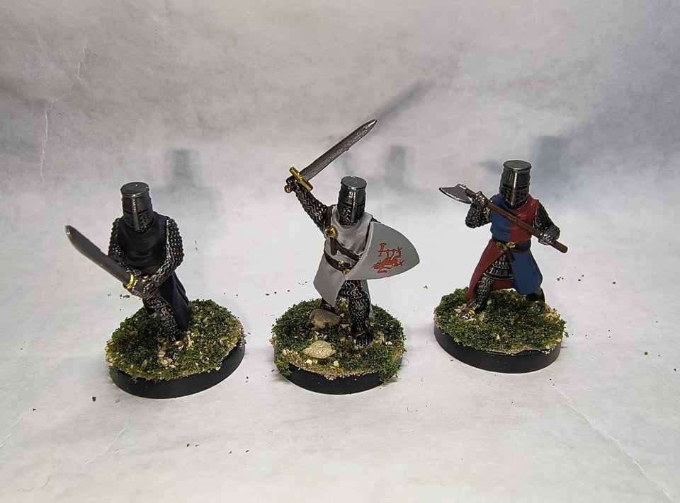 Three knights, from left to right, one with a black surcoat and a falchion, one with a white surcoat and sword and shield, and one with a red and blue surcoat with an axe