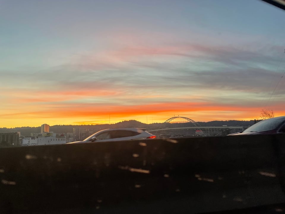 a blurry sunset set of orange yellows and pinks through a car windo A Portland bridge can be seen in the distance