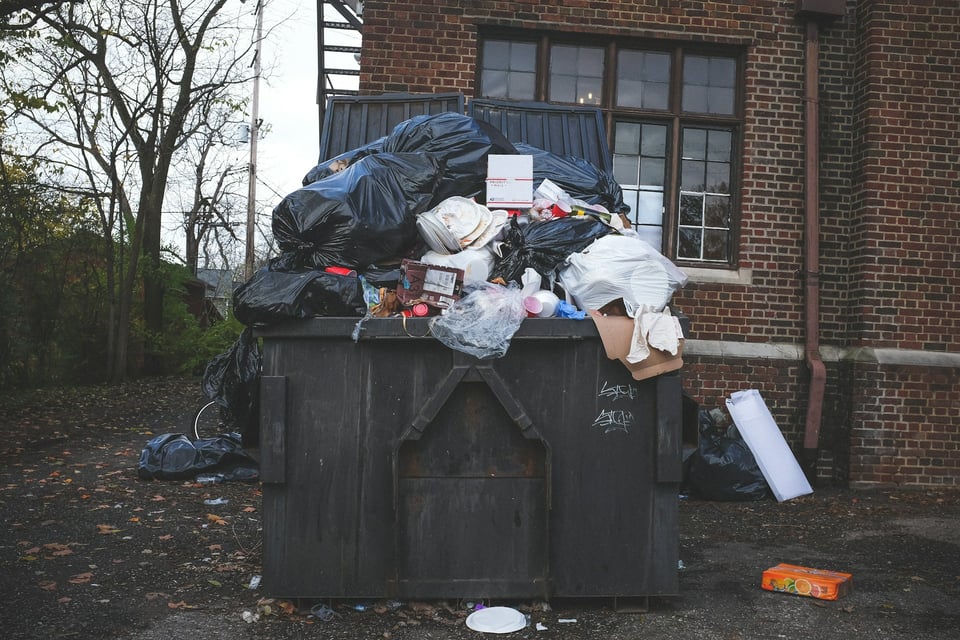 A dumpster, overflowing with trash bags. Photo by Kenny Eliason on Unsplash.