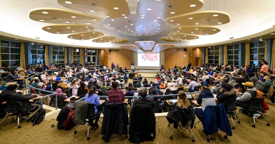 A large lecture in a modern lecture hall, with attendees seated in rows around the speaker