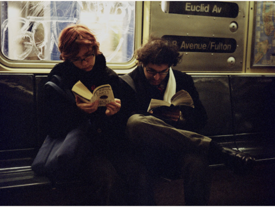 Two riders in the NYC subway, each engrossed in a book.