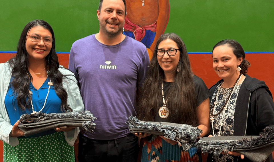 Four people stand in a row, with three of them holding blankets as gifts.