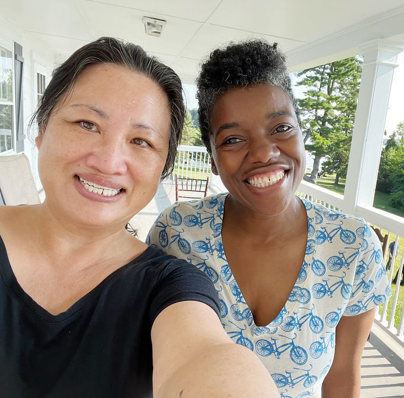 Two women take a selfie on a white balcony with a lake in the background