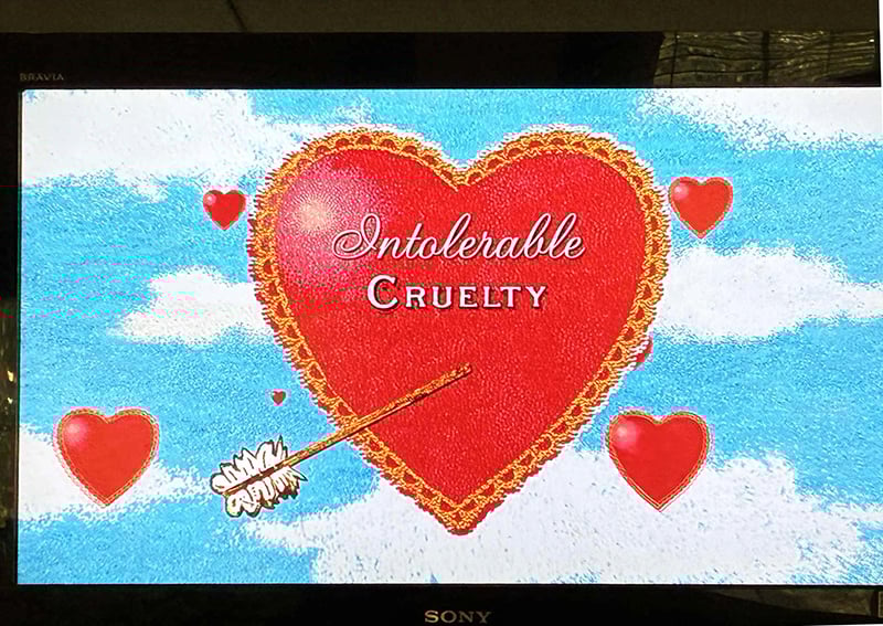 A photo of my television, which in this instant displays the title of the movie Intolerable Cruelty, on a big red heart pierced by Cupid's arrow.