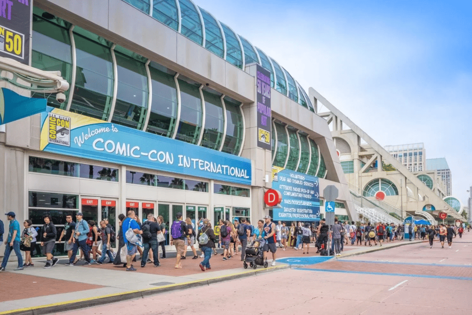 photo of san diego convention center, during the day, with people in front of it and a banner that reads "welcome to comic-con international"