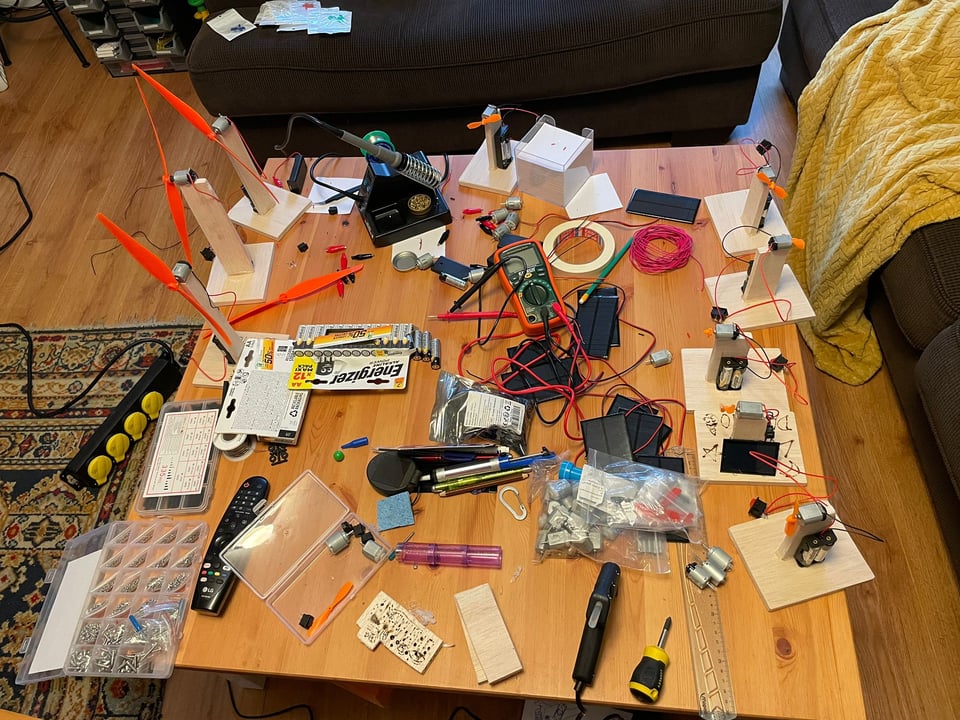 A coffee table filled with tools and electronics and a soldering iron in preparation to build electronic kits for a child's birthday party.