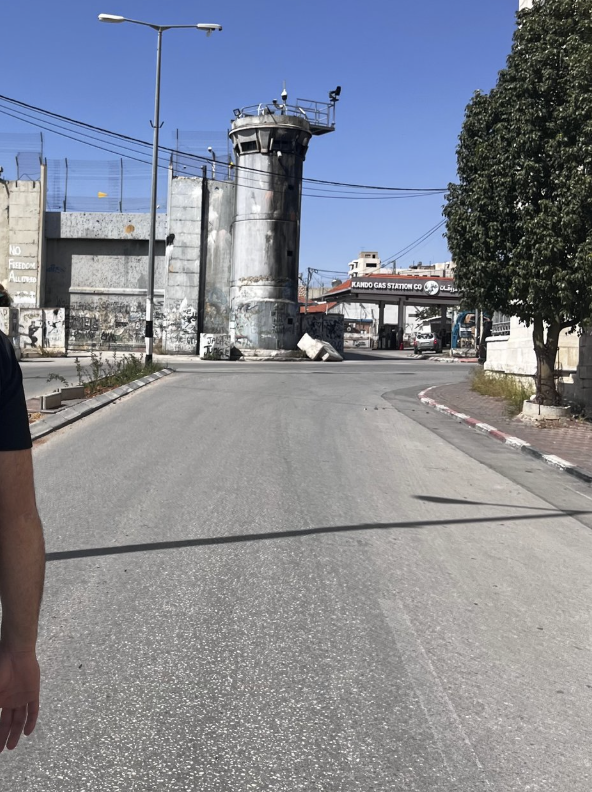 A street facing a large concrete wall and a military tower