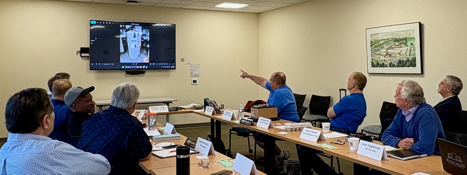 Dale is seated with other members and he’s pointing to an image on the wall-mounted digital display.