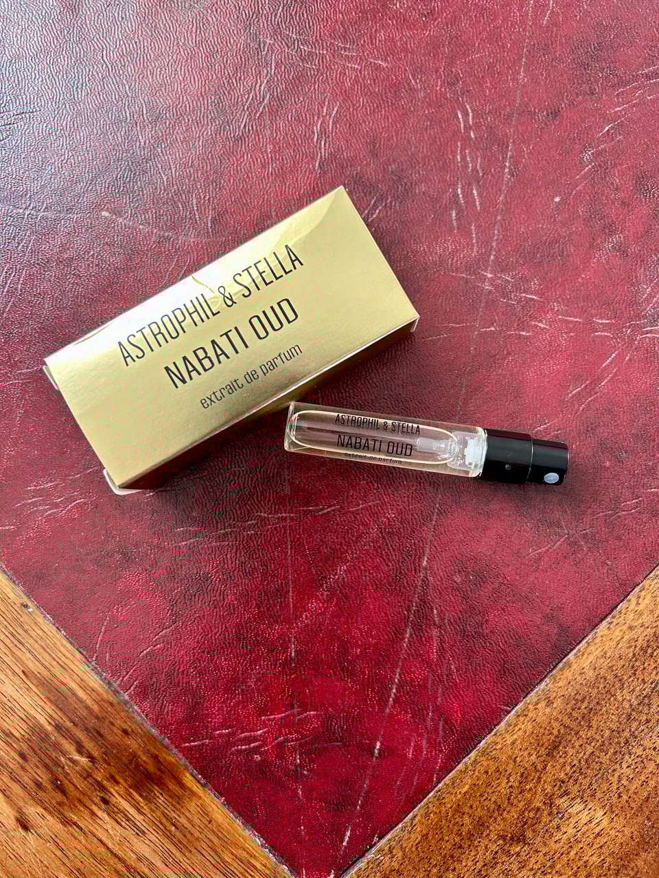 A small glass vial of Nabati Oud perfume by Astrophil and Stella is next to a gold box with their branding on. Everthing is lying on a dark red lether topped table. Image by Rowan Ambrose.