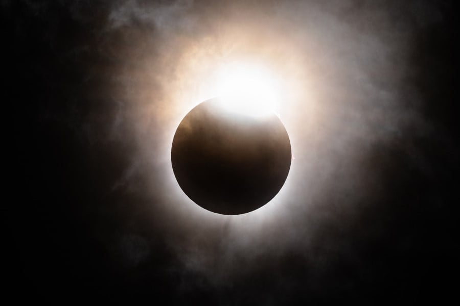 Photo of the moon's descent below the sun's horizon with cloud vapour creating an eerie glow around the eclipse.