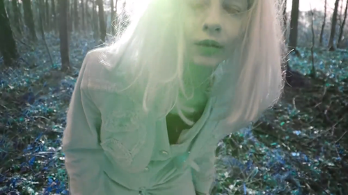 Still from Sara Tuss Efrik's 'Persona Peep Show' – a woman in spectral light in a bleached out forest.