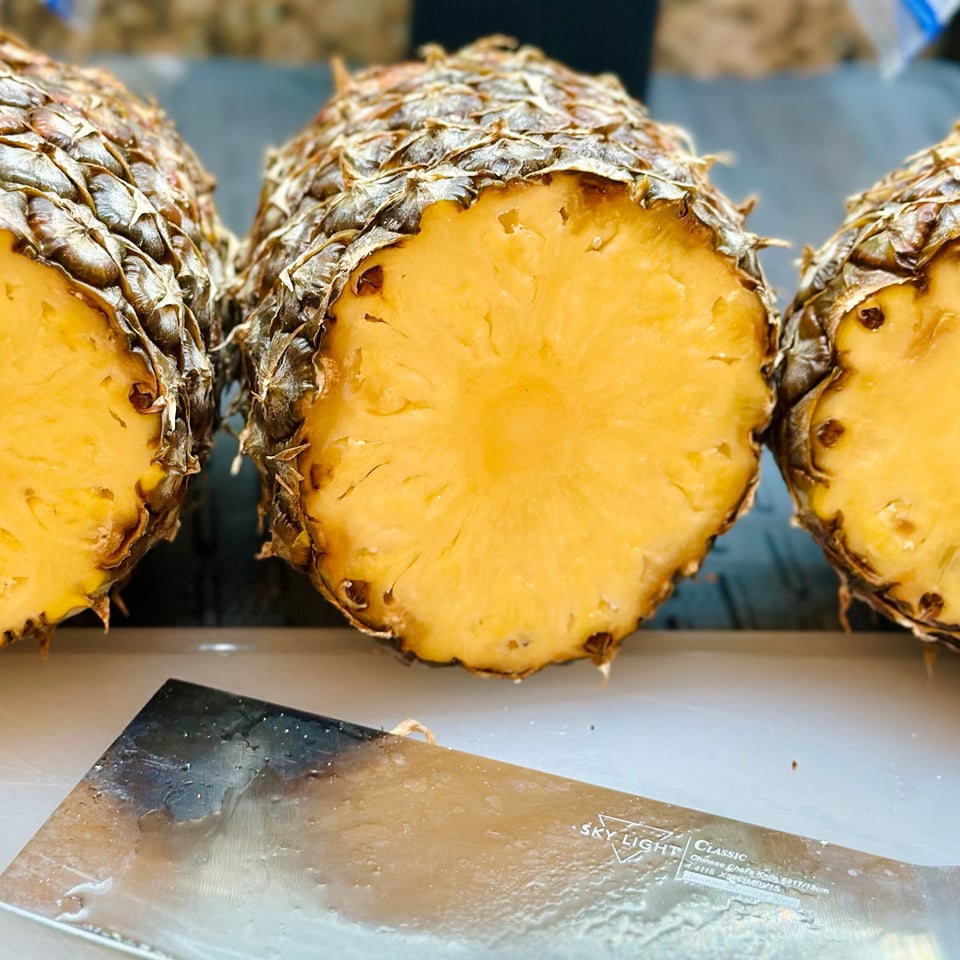 a photo of the cross section of some fresh pineapples on a cutting board, with a cleaver in front of it