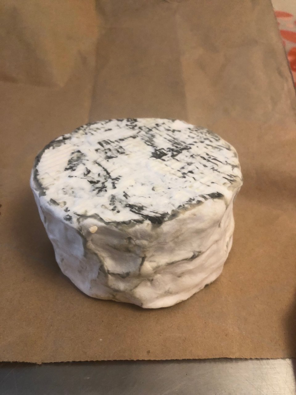a single bloomy-rind cheese with bits of ash poking through the mold sitting upona piece of brown paper