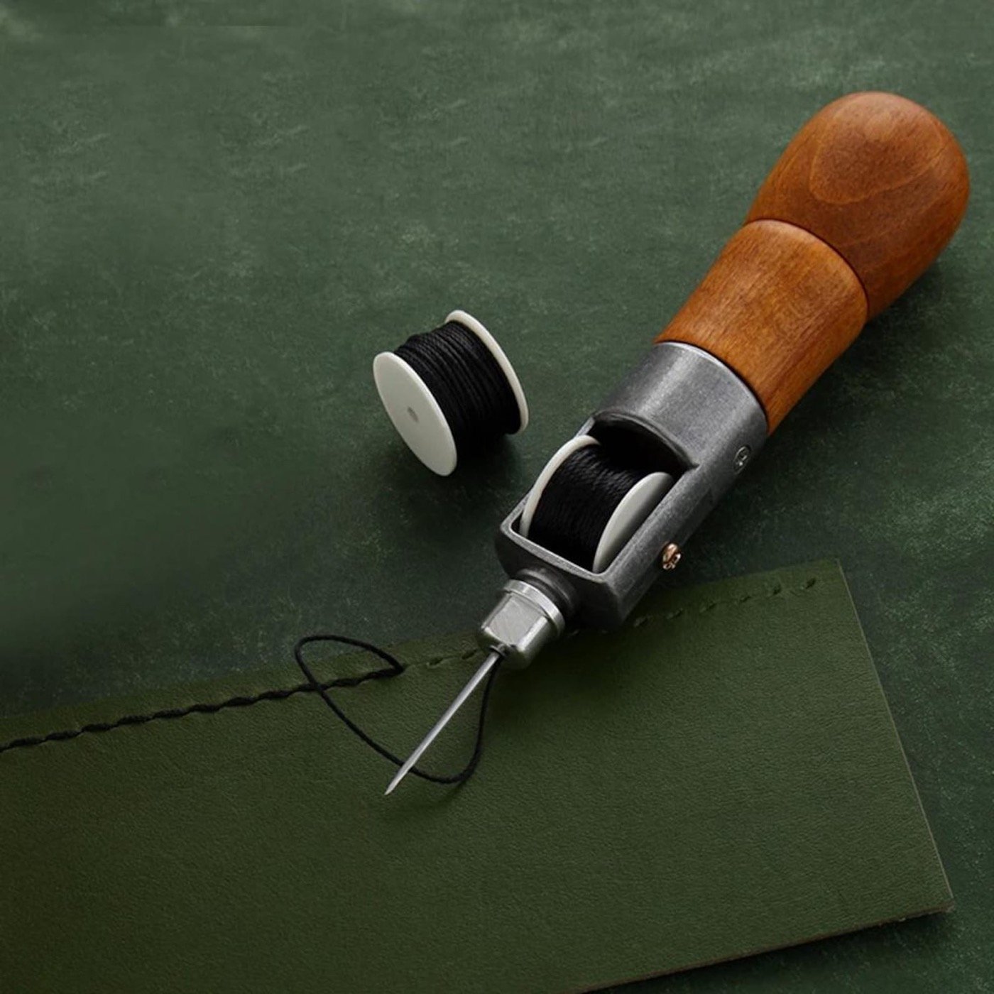 A lockstitch awl with a wooden handle, open bobbin housing, and a spare spool of waxed thread. From CraftsArtSupplies on Etsy.