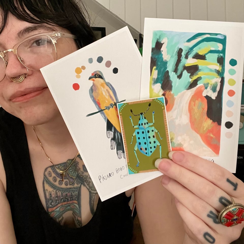 Destiny holds 2 illustrated postcards- one with an abstract landscape and one with a bird- and a beetle sticker.