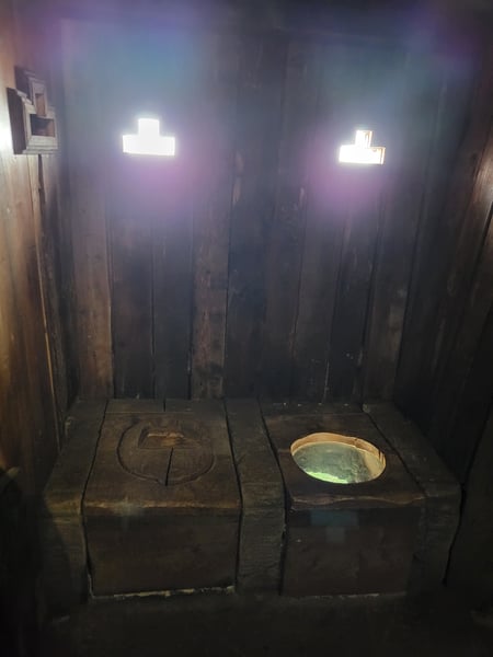 Side-by-side castle toilets, made from wood. Light glows through fake windows behind them.