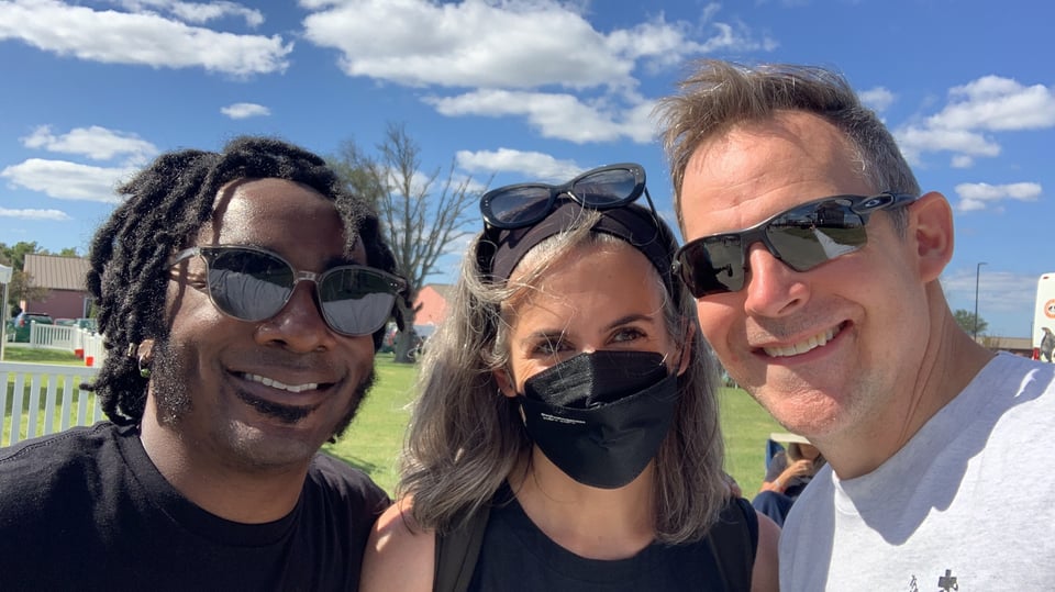 Two men in sunglasses and one woman in a mask posing for an outdoor selfie 