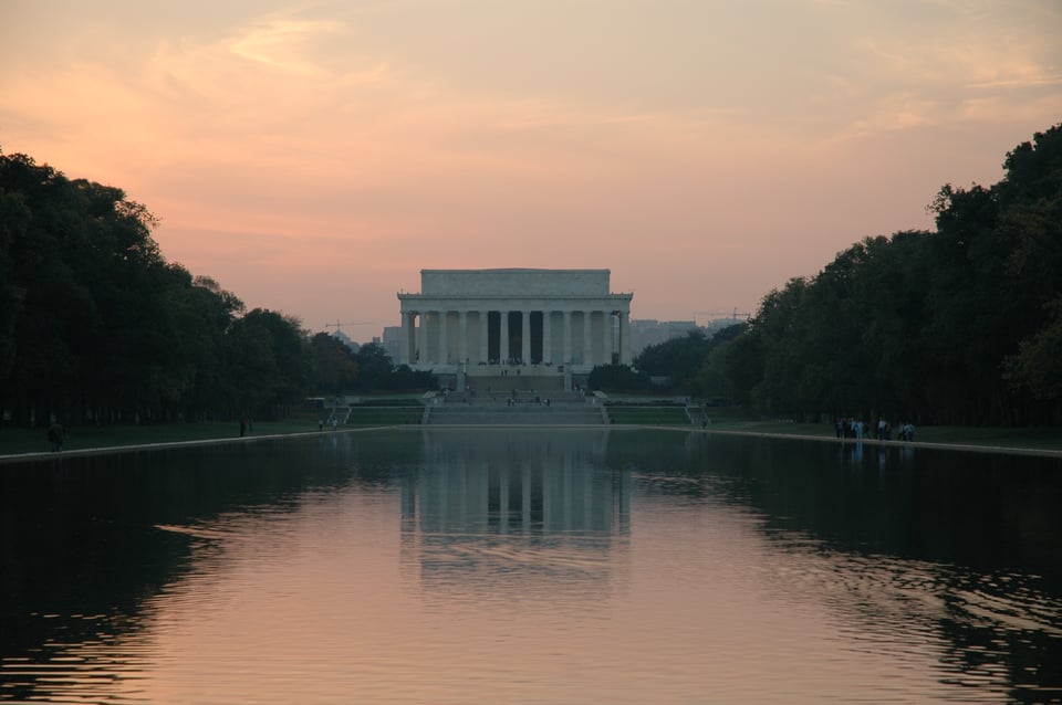 The marble Lincoln Memorial sits at the far end of the Reflecting Pool at dusk, where its reflection is seen in the water.