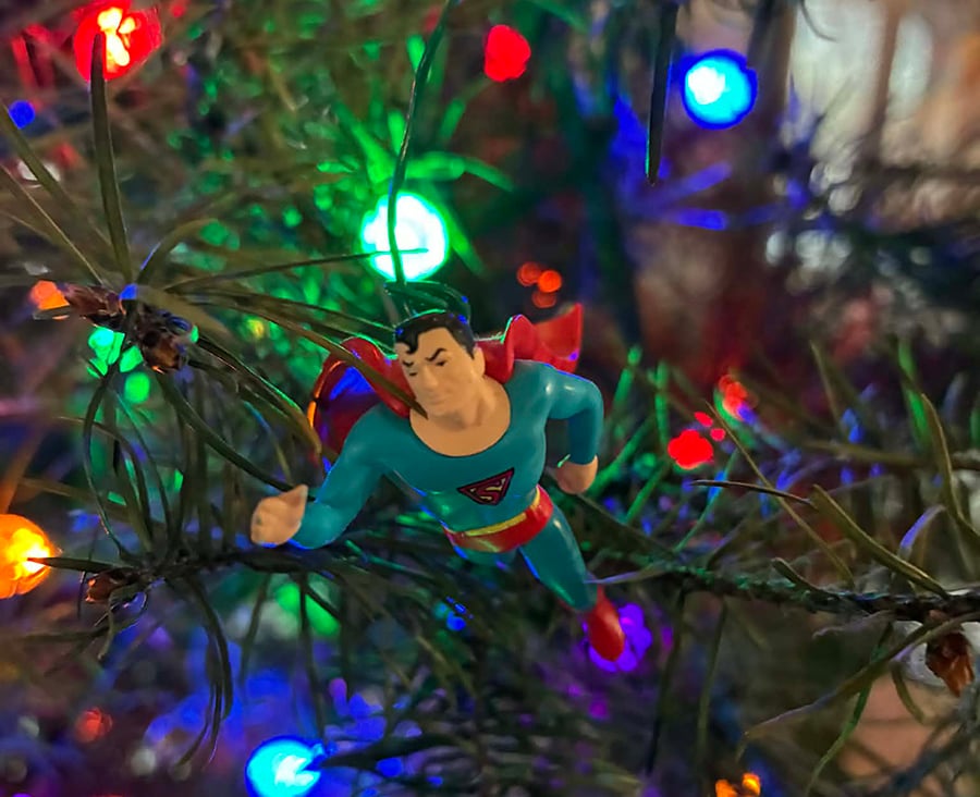 This is a close-up photo of a Superman ornament hanging from my Christmas tree. You can tell it's a Christmas tree from the pine needles and the colorful lights. It's an old-fashioned style Superman--his S shield is a triangle, so he looks like he's from the 30s, maybe early 40s.