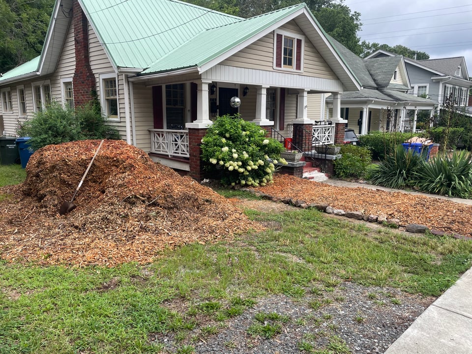 a 1920s bungalow with a green roof with a large pile of mulch outside