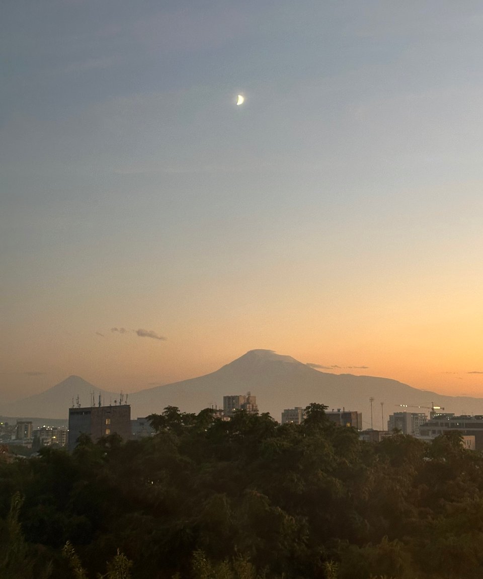 Mount Ararat over the rooftops of Yerevan at sunset, with a crescent moon