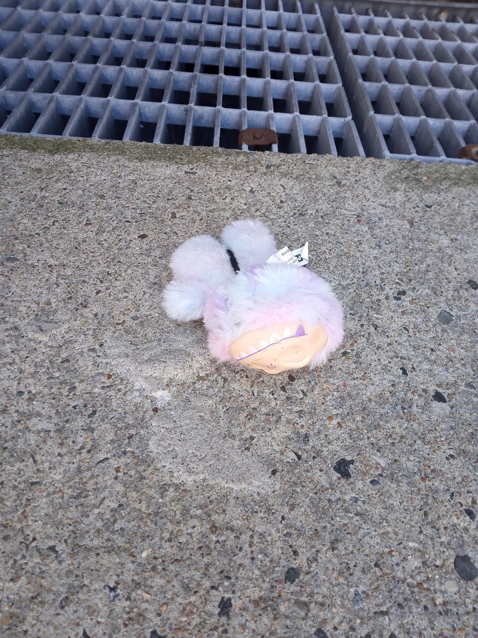 A pale purple Labubu, twisted and eyeless on a sidewalk.
