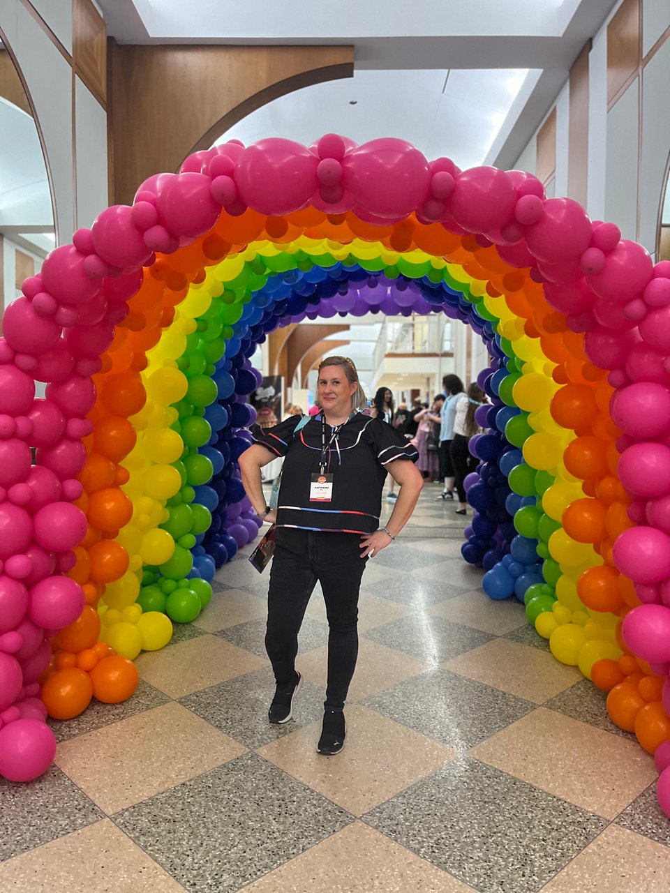 Ya girl under a rainbow balloon arch