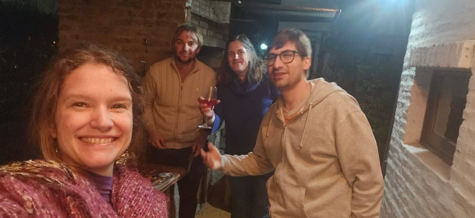 Four adults smile at the camera - one holding up a glass.