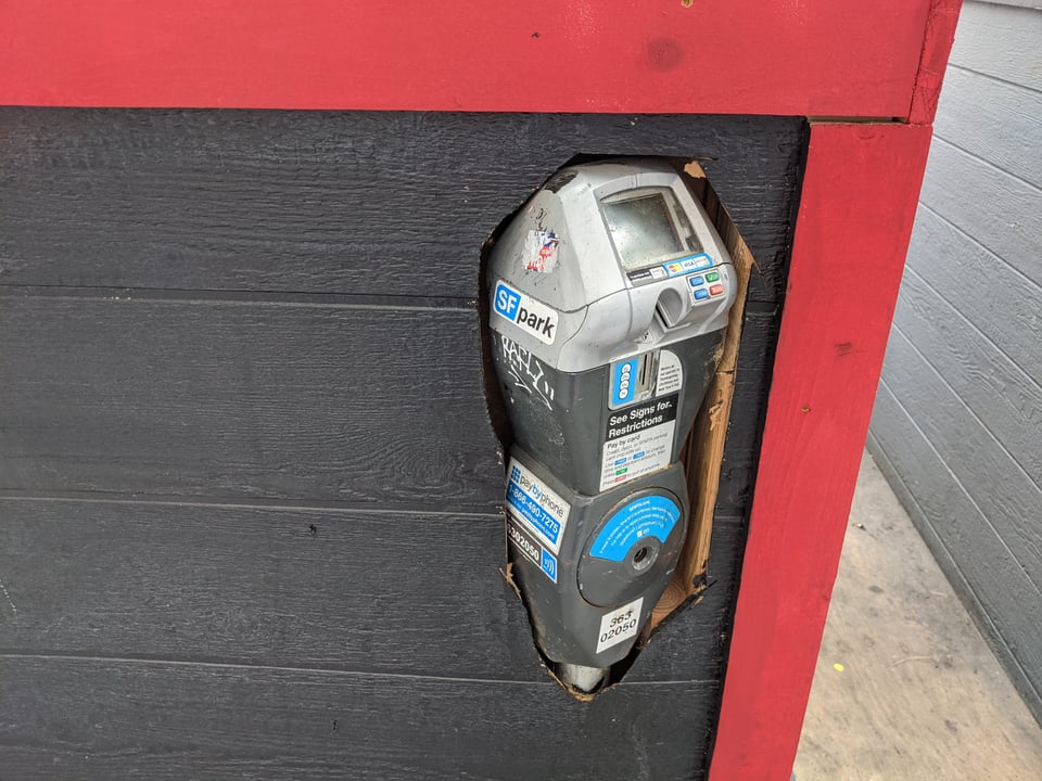 A parking meter trapped inside a parklet for outdoor dining, with the head of the parking meter poking through