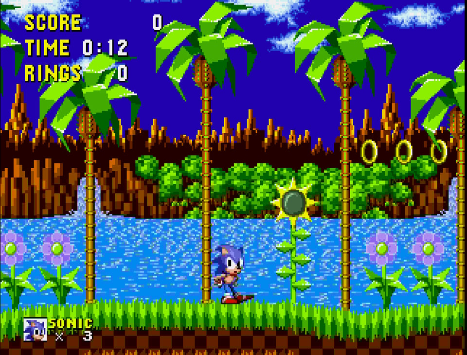 A screenshot from the Green Hill Zone level of Sonic the Hedgehog. Sonic, a blue pixel art hedgehog, stares quizzically at the viewer. He stand in front of a body of water, green hills, flowers and golden rings, all evoked in a similar pixel art style.