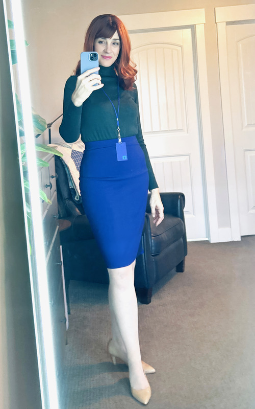 A selfie of me in my Halloween costume dressed as Helly R. from the TV show, Severance. I'm wearing a red wig, green turtleneck, and a blue skirt. I have a Lumon ID card around my neck.