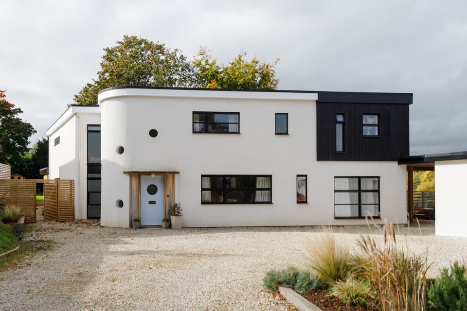 What looks like a modernised 1930s building, with black framed windows set into cream-painted render. One end of he building is curved, with porthole windows and a stone entranceway.