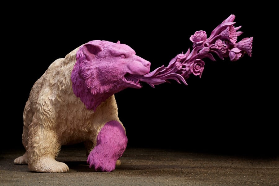 Sculpture of a bear, it’s body white, but its left foreleg and head a rich pink colour, with a bouquet of flowers streaming from its mouth.