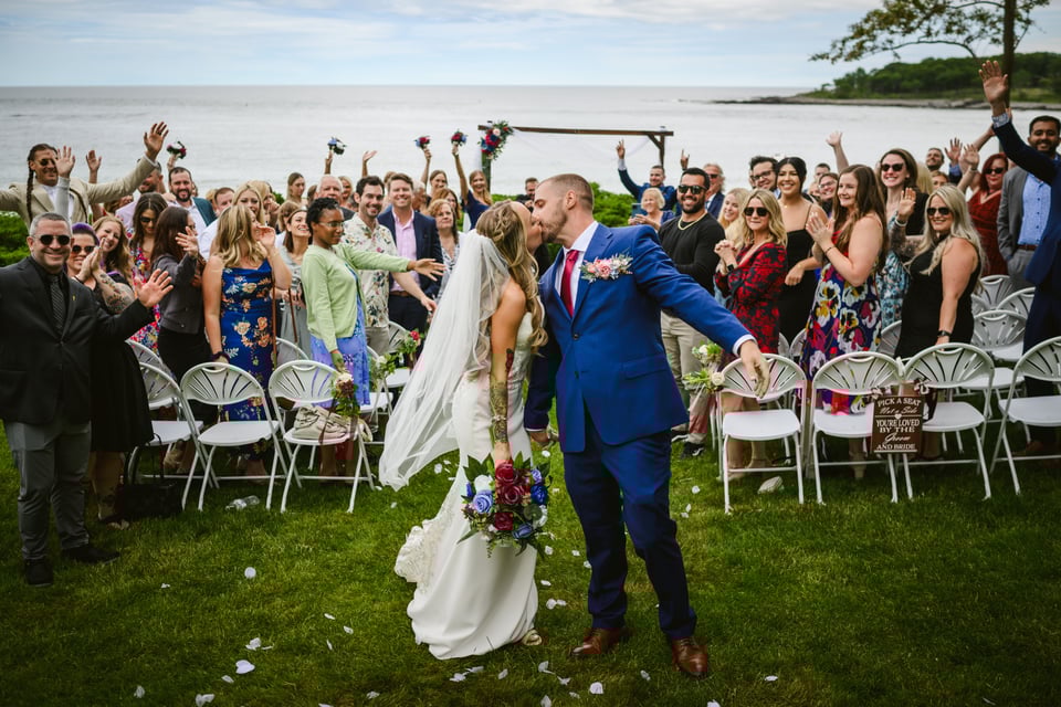 Bride and groom kissing each other during their wedding processional while all the wedding attendees cheer for them