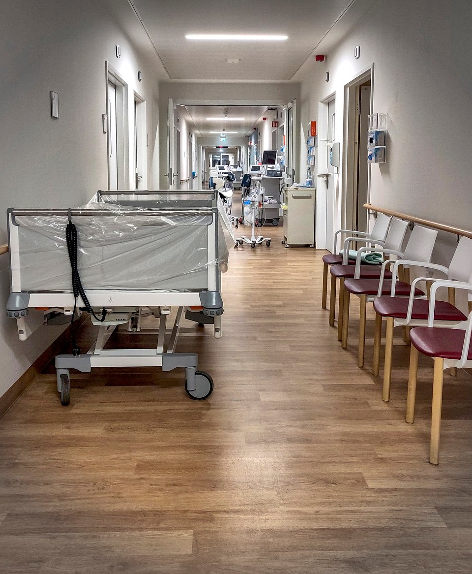 Blick in einen menschenleeren Krankenhausflur, in dem Betten und Gerätschaften stehen.
