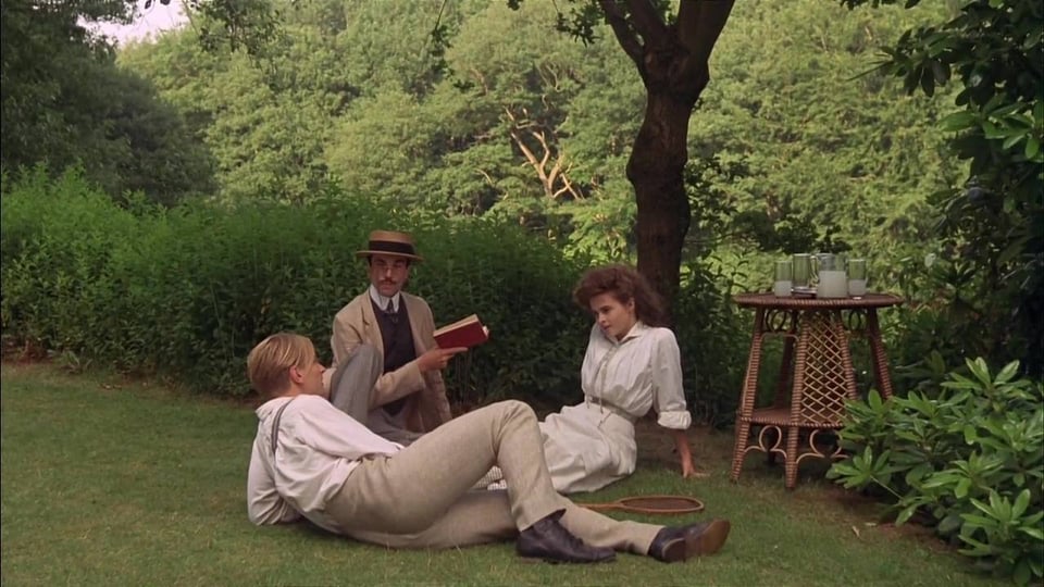 Three characters from the film A Room with a View are sitting on the grass.
