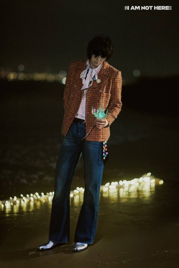 Wang Yibo standing by a row of lit candle lights at night, in a stunning pair of silver shoes, gorgeous flared blue jeans, a beautiful orange-red chanel jacket over a silky white/pink-ish shirt with a giant pussy bow, and a scarf with a bright colorful boxy pattern being used as a belt with one end dangling from his waist. There's also a brooch and a watch chain. And to all this he's holding a bright LED-lit green flower in his hand, looking down at it introspectively, his bob dylan fringe shadowing his eyes. He's breathtaking.