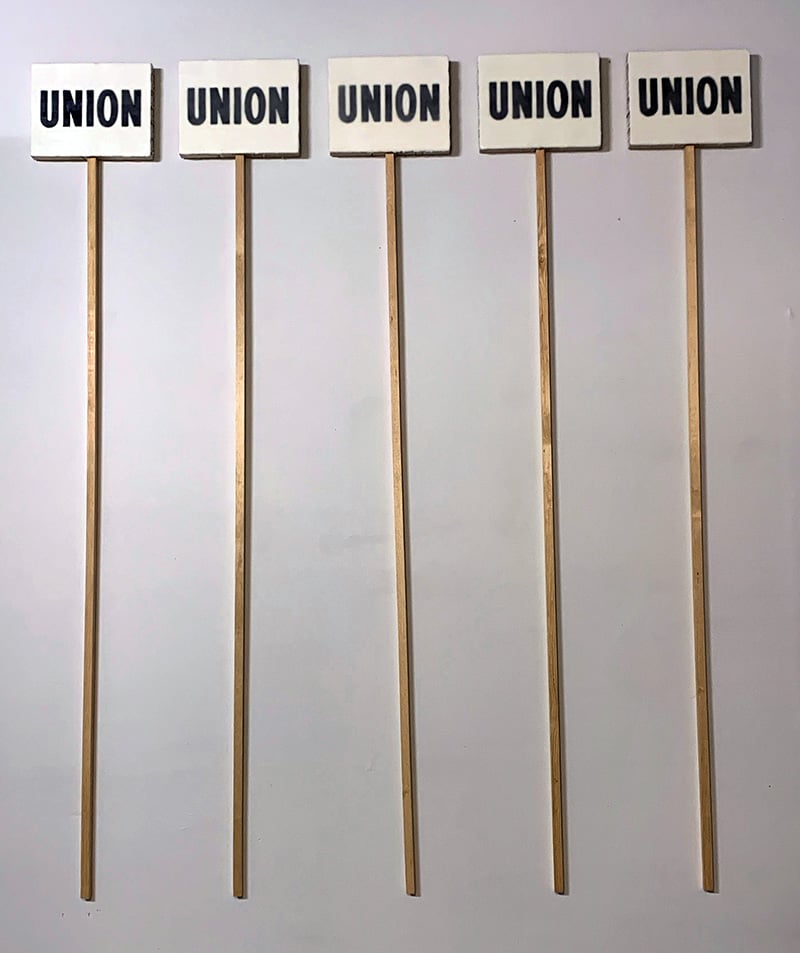 5 paintings that say UNION with very long sticks attached. They look like union signs.