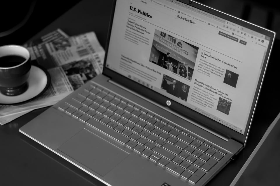 A laptop open to a news site, with a cup of coffee off to the side. Photo by Anna Keibalo on Unsplash