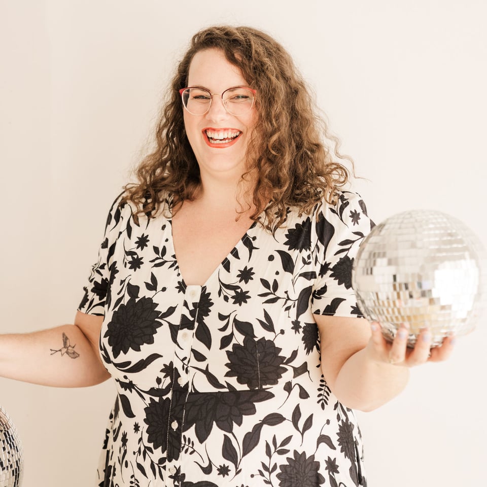 Photo of Amelia Hruby holding a disco ball and smiling at the camera